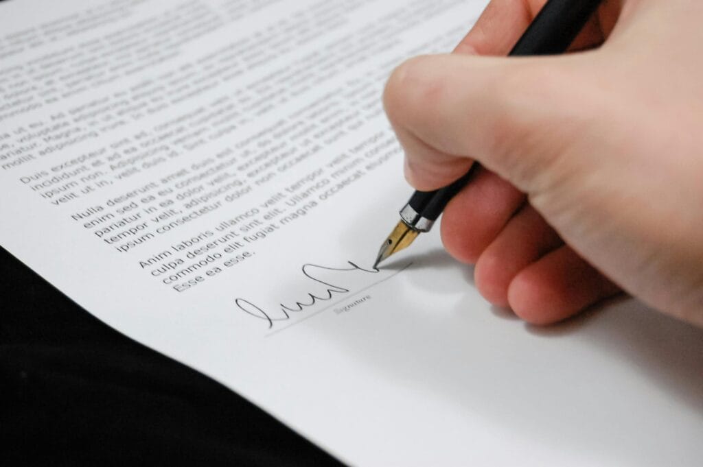 Nahaufnahme einer Hand, die ein juristisches Dokument mit einem Füllfederhalter unterzeichnet, was Unterschrift und Zustimmung symbolisiert.