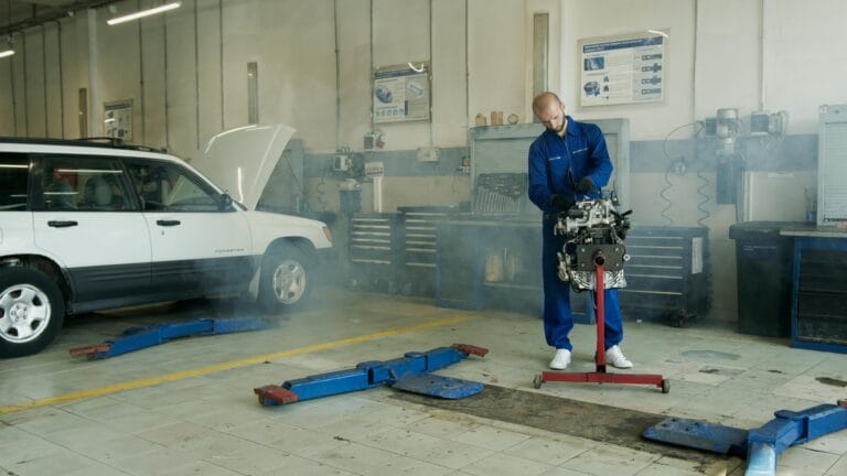Mecánico con mono azul trabajando en el motor de un coche en un taller de reparación de automóviles con un coche blanco.